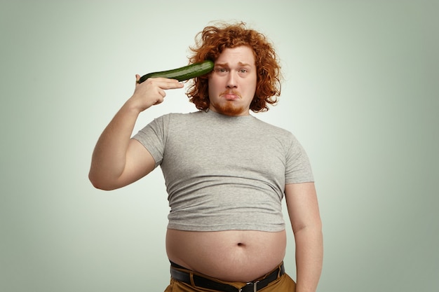 Hombre pelirrojo joven con sobrepeso obeso listo para dispararse fuera de pistola de pepino improvisado