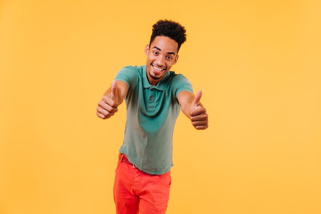 Hombre de pelo corto divertido posando con los pulgares para arriba. Foto interior de chico africano feliz en traje de moda.