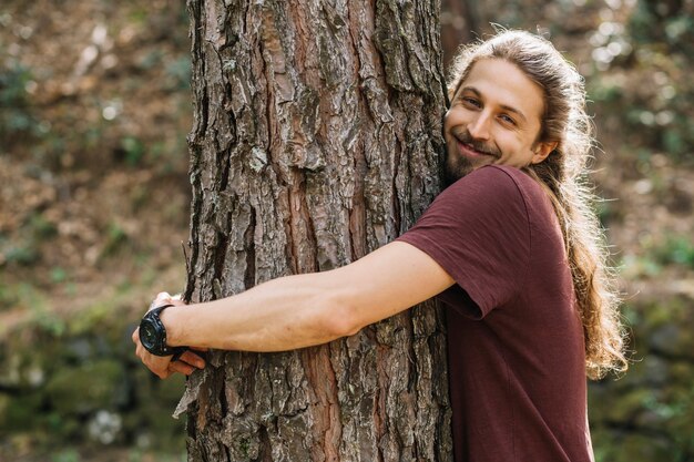 Hombre con pelo largo abrazando un árbol