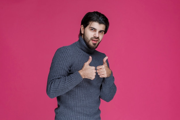 Hombre con pelo largo y barba haciendo pulgar arriba signo de mano.