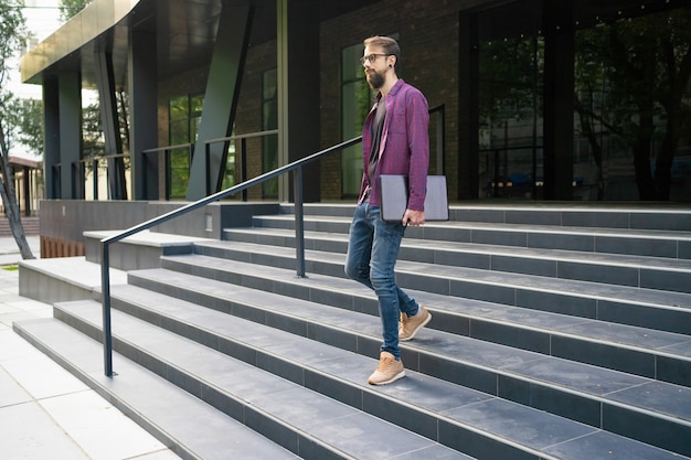 Hombre de pelo oscuro bajando escaleras y sosteniendo portátil