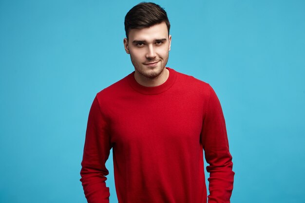 Hombre de pelo oscuro joven guapo vistiendo elegante suéter rojo con mangas largas sonriendo a la cámara