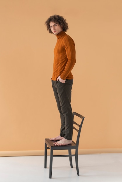 Hombre de pelo rizado con blusa marrón posando en silla