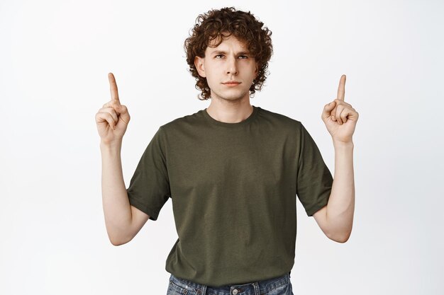 Hombre de pelo rizado molesto señalando con el dedo hacia arriba mirando el anuncio de lectura del logotipo con expresión de cara irritada fondo blanco