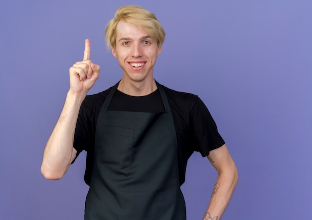 Hombre de peluquero profesional en delantal sonriendo mostrando el dedo índice con nueva idea