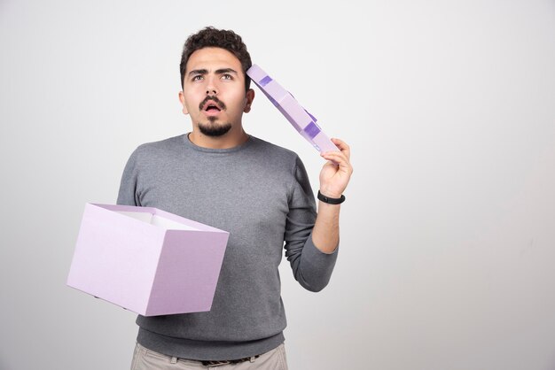 Hombre pensativo con una caja violeta abierta sobre una pared blanca.