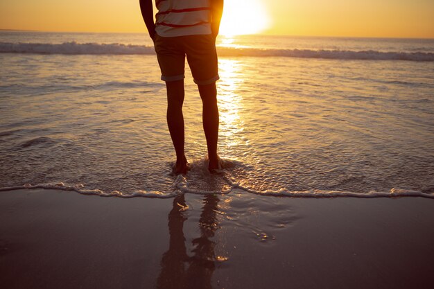 Hombre pensativo de pie con las manos en el bolsillo en la playa