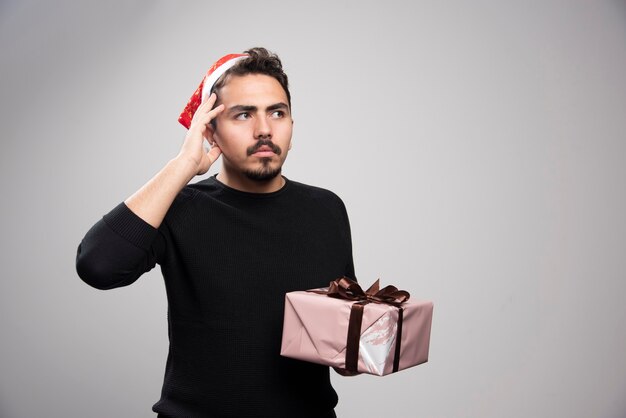 Un hombre pensativo con un sombrero de Santa sosteniendo un regalo de año nuevo.