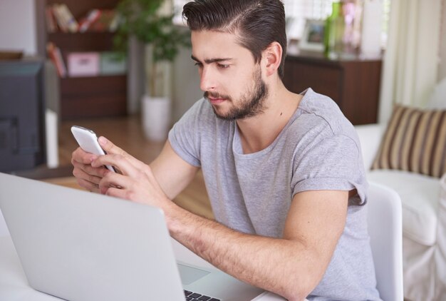 Hombre pensativo trabajando en su teléfono inteligente y computadora portátil