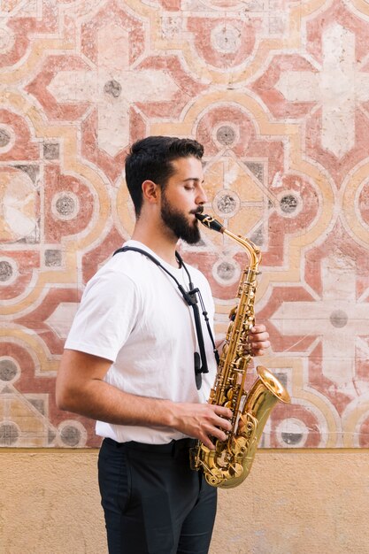 Hombre de perfil y de pie tocando el saxofón sobre un fondo geométrico