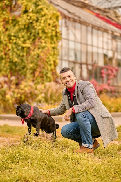 Un hombre con un perro negro en el parque de otoño.