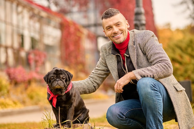 Un hombre con un perro negro en el parque de otoño.