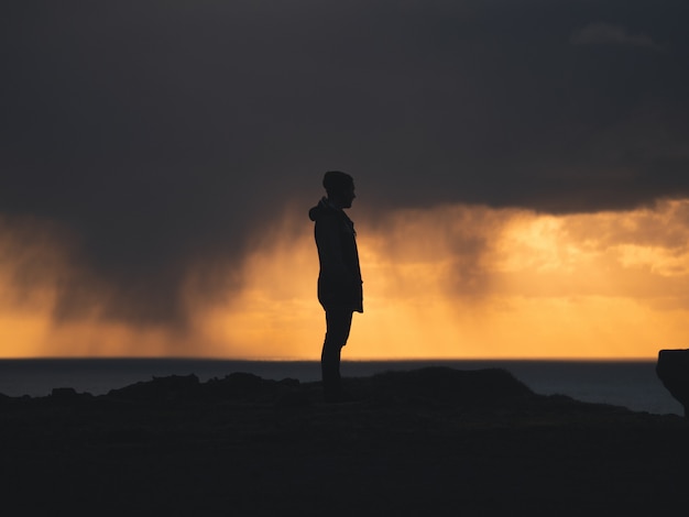 Foto gratuita hombre de pie en un acantilado con un cielo amarillo y nublado en el fondo