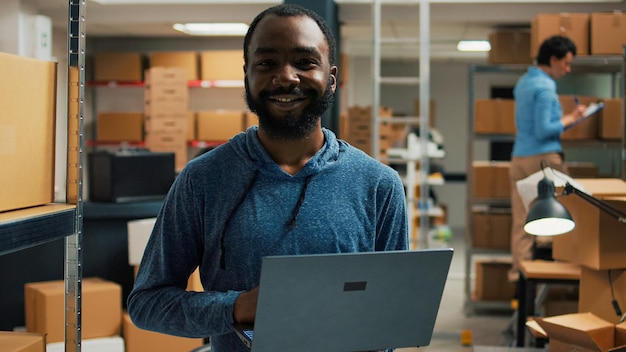 Foto gratuita un hombre está de pie en un almacén con una computadora portátil en la mano.