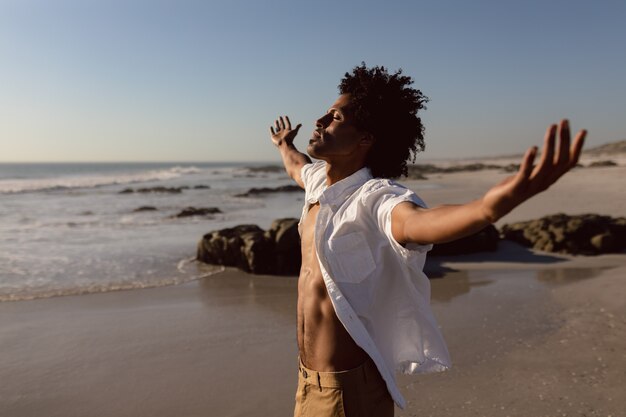 Hombre de pie con los brazos extendidos en la playa