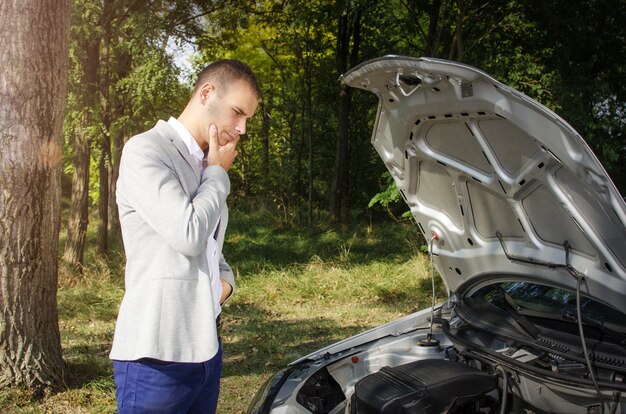 Hombre de pie en la carretera junto al coche roto y pensando cómo arreglarlo