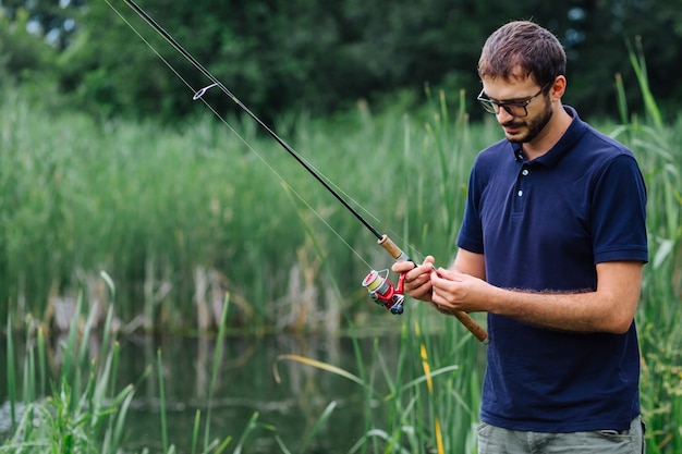 Hombre de pie cerca del lago que ata el cebo de pesca en la barra