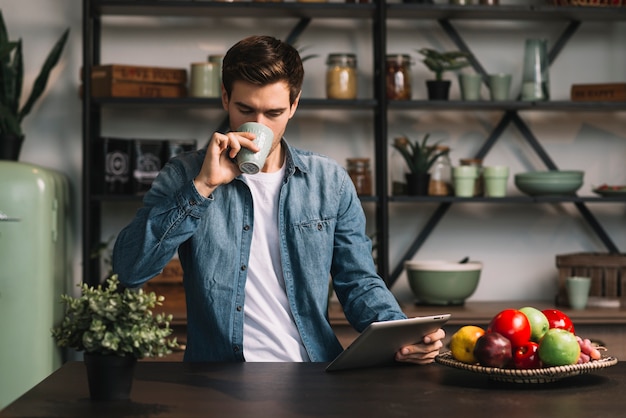 Foto gratuita hombre de pie en la cocina tomando café con tableta digital