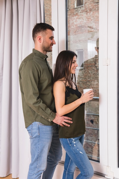 Hombre de pie detrás de su novia sosteniendo la taza de café en la mano