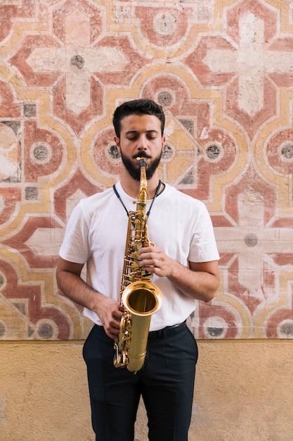 Foto gratuita hombre de pie y de frente tocando el saxofón sobre un fondo geométrico