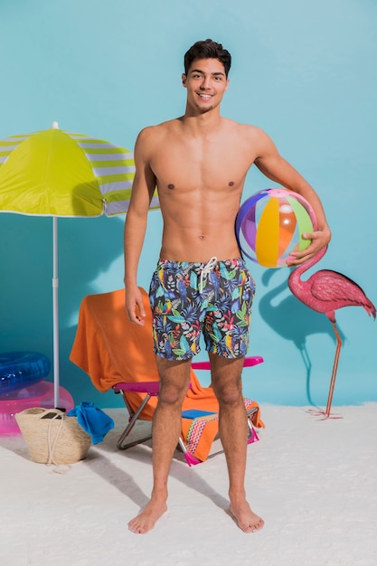 Hombre de pie joven en traje de baño sosteniendo la bola inflable
