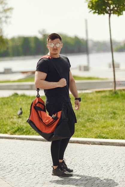 Hombre de pie junto al agua. Chico en ropa deportiva. Hombre en un parque de verano con mochila