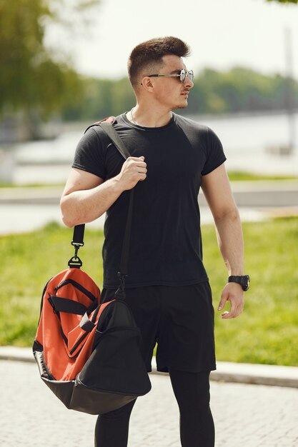 Hombre de pie junto al agua. Chico en ropa deportiva. Hombre en un parque de verano con mochila