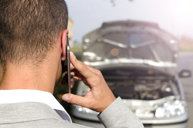 Hombre de pie junto al vehículo roto llamando al servicio de remolque