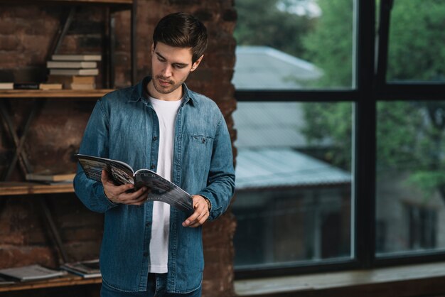 Hombre de pie junto a la estantería leyendo revista.