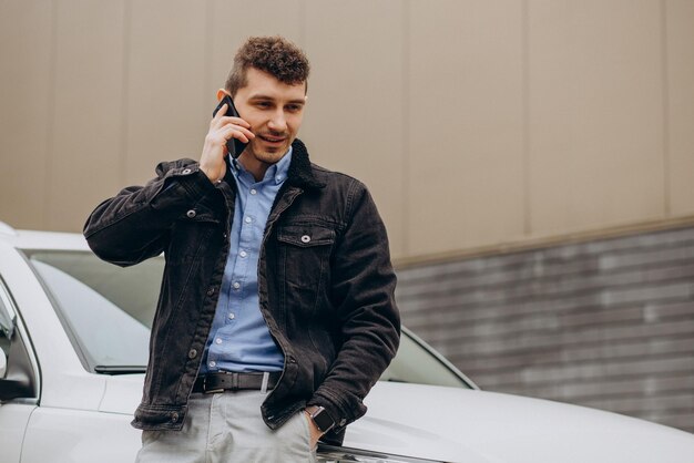 Hombre de pie junto a su coche y hablando por teléfono