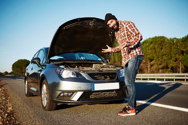 Hombre de pie junto a su coche roto