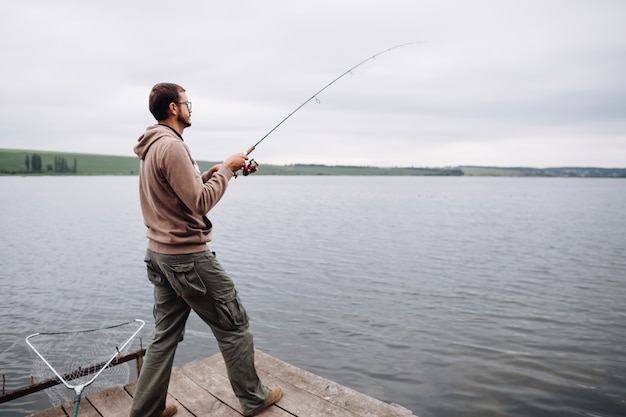 Hombre de pie en el muelle de pesca en el lago