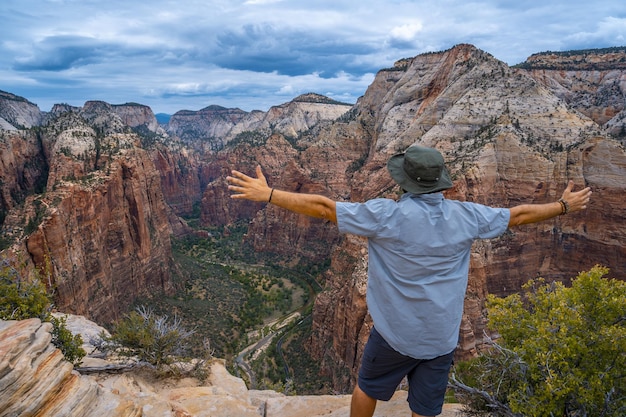 Hombre de pie en la parte superior de las formaciones rocosas con los brazos estirados en el Parque Nacional Zion, EE.UU.