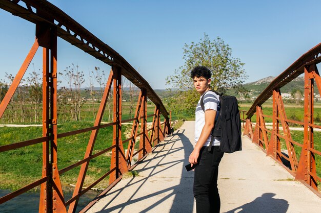 Hombre de pie en el puente mirando a la cámara con teléfono móvil