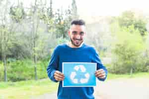 Foto gratuita hombre de pie con el símbolo de reciclaje en el bosque