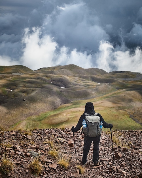 Hombre de pie sobre una colina mientras disfruta de la vista con un cielo nublado