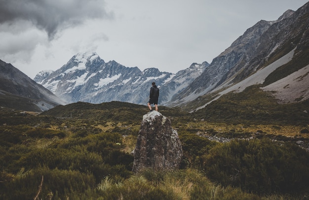 Hombre de pie sobre la piedra en Hooker Valley Track con vistas al monte Cook en Nueva Zelanda