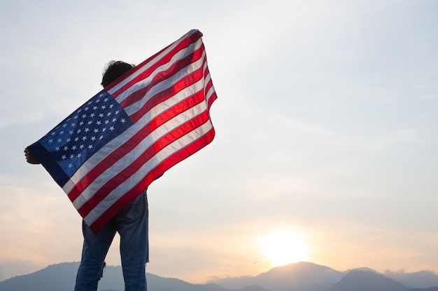 Foto gratuita hombre de pie y sosteniendo la bandera de estados unidos en la vista del amanecer