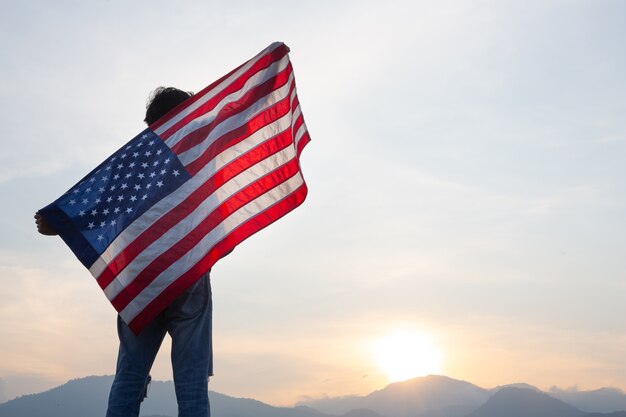 Hombre de pie y sosteniendo la bandera de Estados Unidos en la vista del amanecer