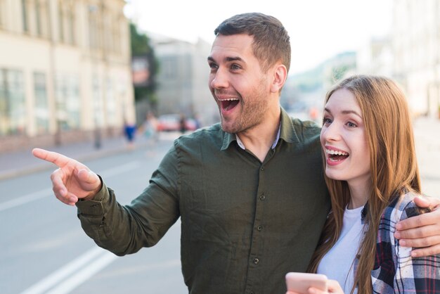 Hombre de pie con su novia apuntando a algo en la calle