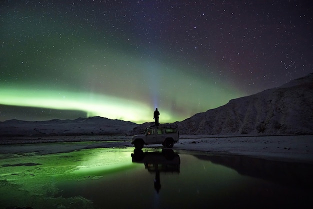 Hombre de pie en SUV mirando la aurora boreal