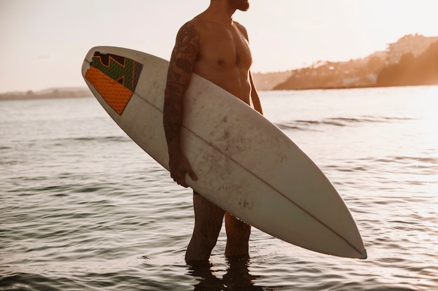 Foto gratuita hombre de pie con tabla de surf en el mar