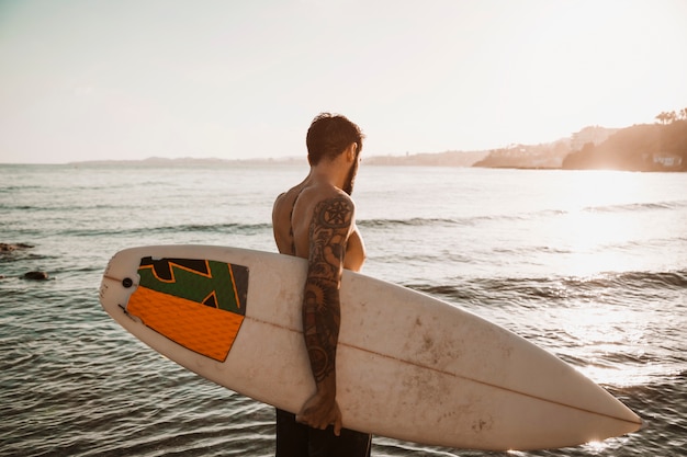 Foto gratuita hombre de pie con tabla de surf en la playa