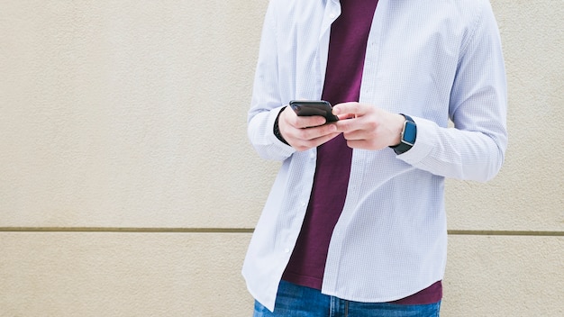 Foto gratuita hombre de pie con teléfono celular frente a muro de hormigón