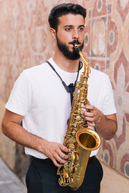 Foto gratuita hombre de pie tocando el saxofón sobre fondo geométrico