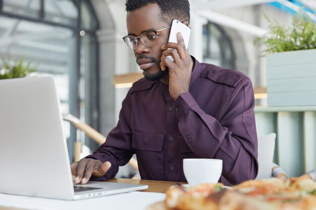 Hombre de piel oscura concentrado en ropa formal mira con confianza en la computadora portátil, tiene expresión seria