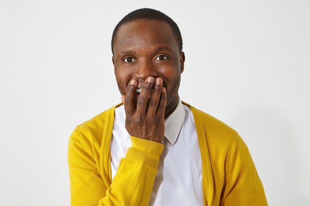 Hombre de piel oscura emocionado feliz cubriendo la boca con la mano, no puedo creer las asombrosas noticias positivas. Retrato de atractivo emocional chico africano vistiendo ropa elegante sonriendo con entusiasmo