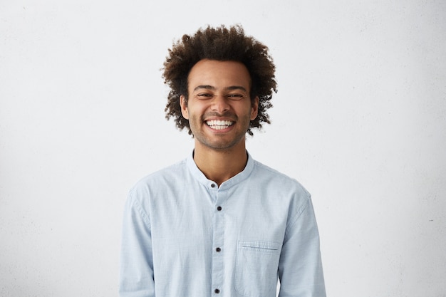 Hombre de piel oscura joven sin afeitar guapo riendo a carcajadas