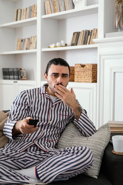 Foto gratuita hombre en pijama viendo la televisión y sosteniendo el control remoto