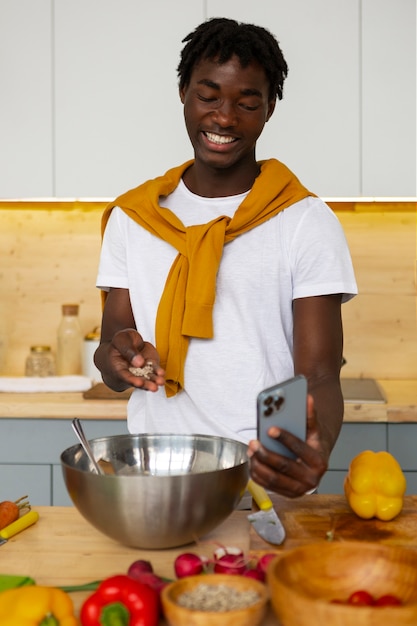 Hombre de plano medio cocinando con teléfono inteligente